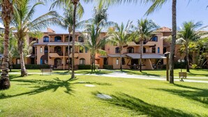 A hotel with multiple balconies, palm trees, and a well-maintained lawn. - Apt in Condo With Pool Near the Beach Gsh0101 (Camaçari)