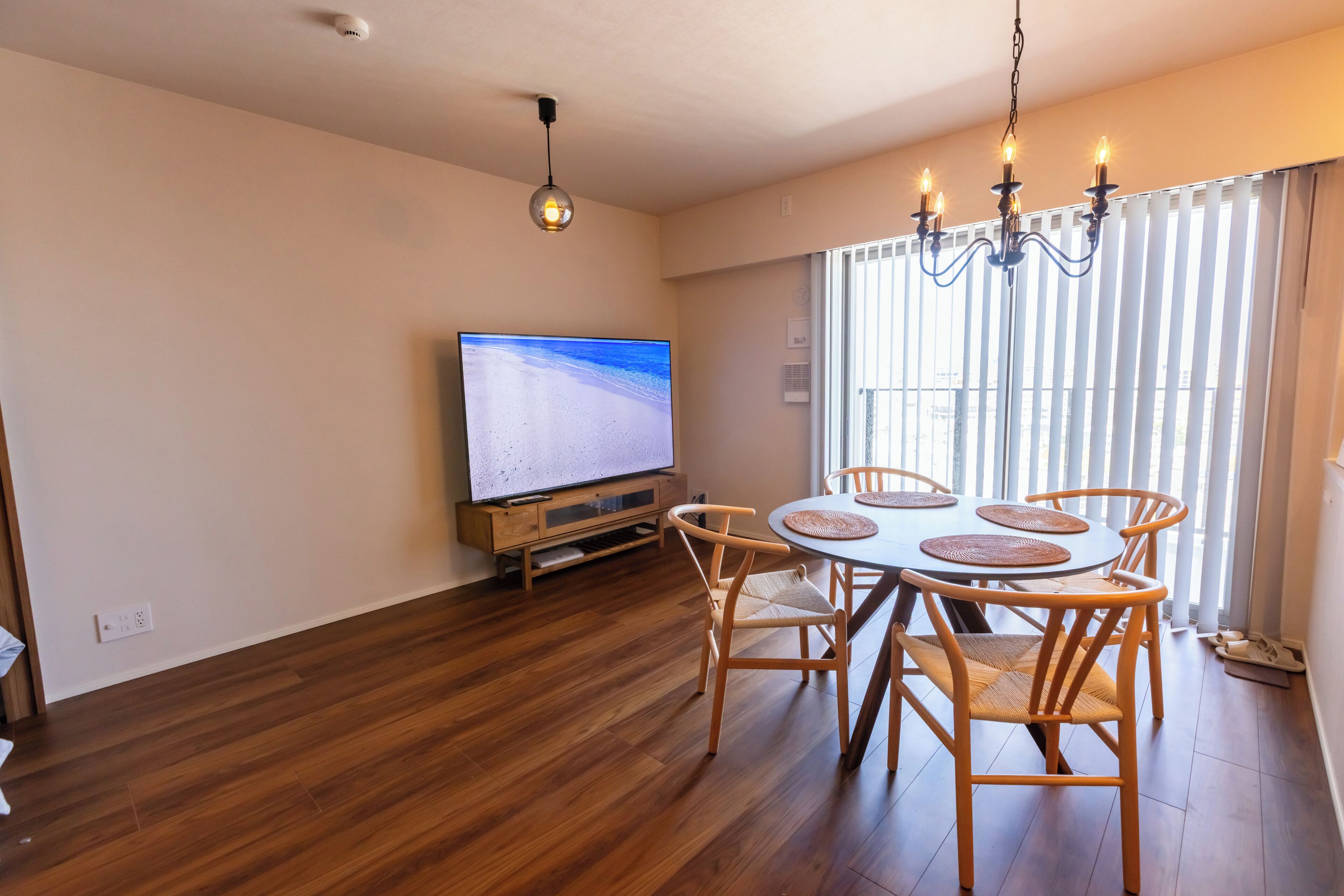 A dining area with a wooden table and chairs, a television on a stand, and a chandelier.