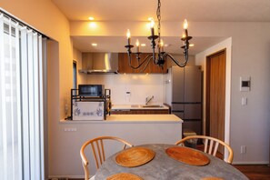A modern kitchen with a built-in microwave, stove, and refrigerator. There is a dining area with a table and chairs. - Buranshiera Naha Kainan Puremisuto 1207 (Naha)