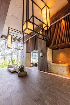 A modern lobby with a reception desk, seating area, and a large window with a view of greenery. - Buranshiera Naha Kainan Puremisuto 1207 (Naha)