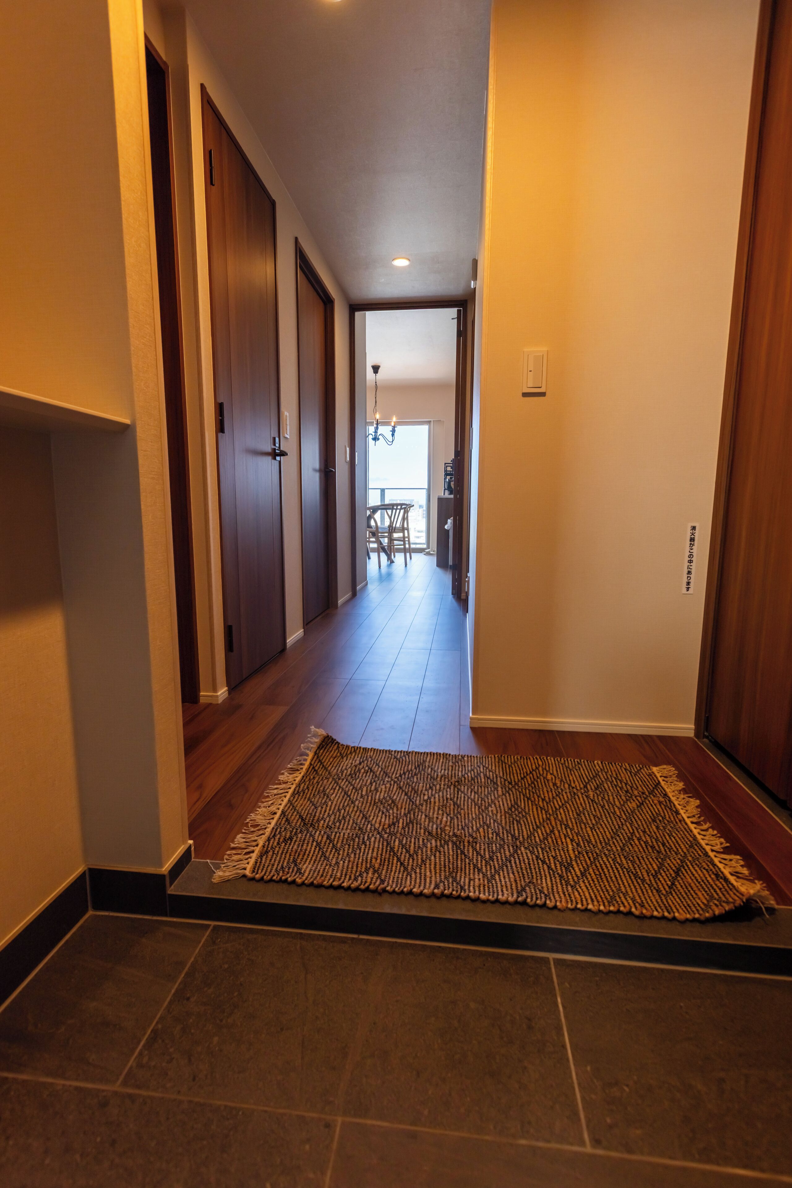 Un pasillo con puertas de madera, un tapete y vista a una habitación con una silla y una mesa.