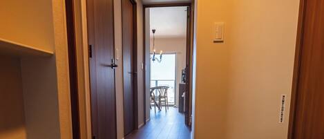 Un pasillo con puertas de madera, un tapete y vista a una habitación con una silla y una mesa.