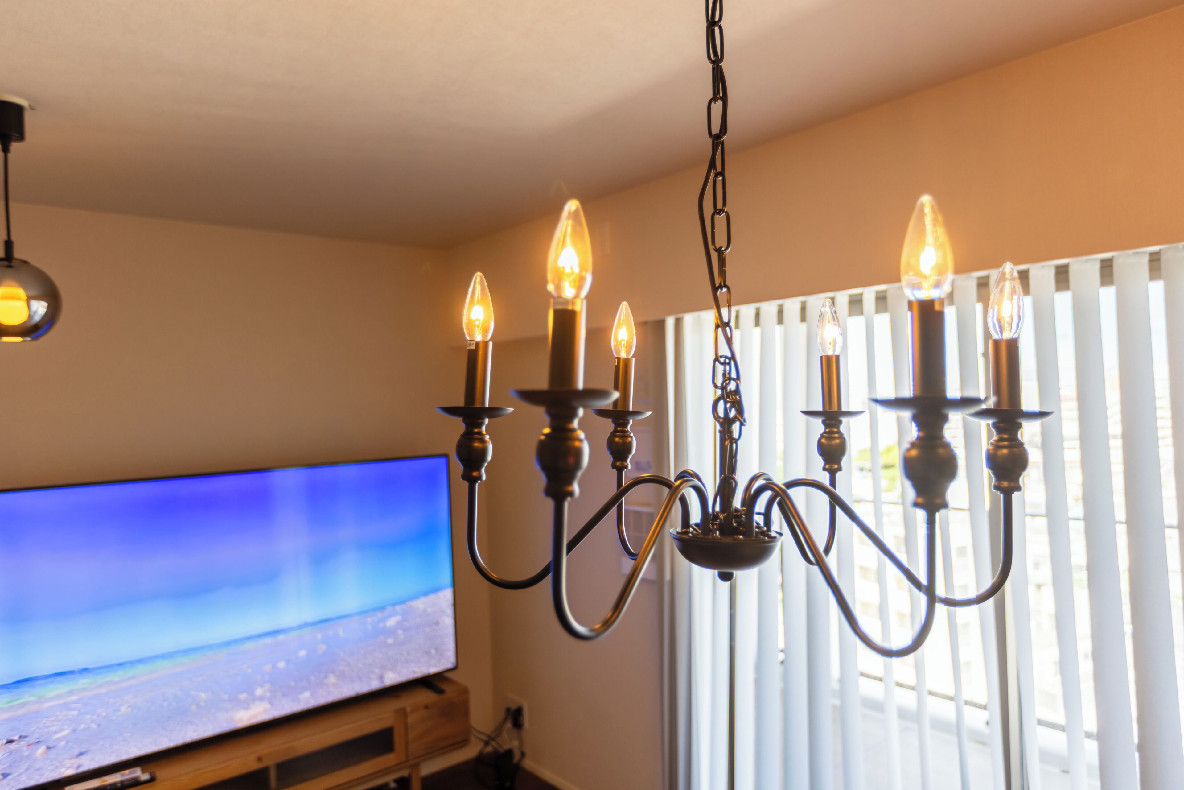 A chandelier with multiple light bulbs, a television on a stand, and a window with blinds.