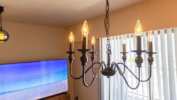 A chandelier with multiple light bulbs, a television on a stand, and a window with blinds.