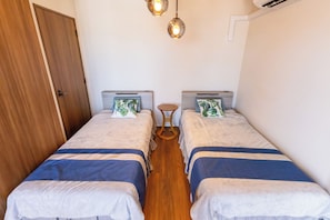 Une petite chambre propre, avec deux lits simples, une porte en bois et une table ronde.