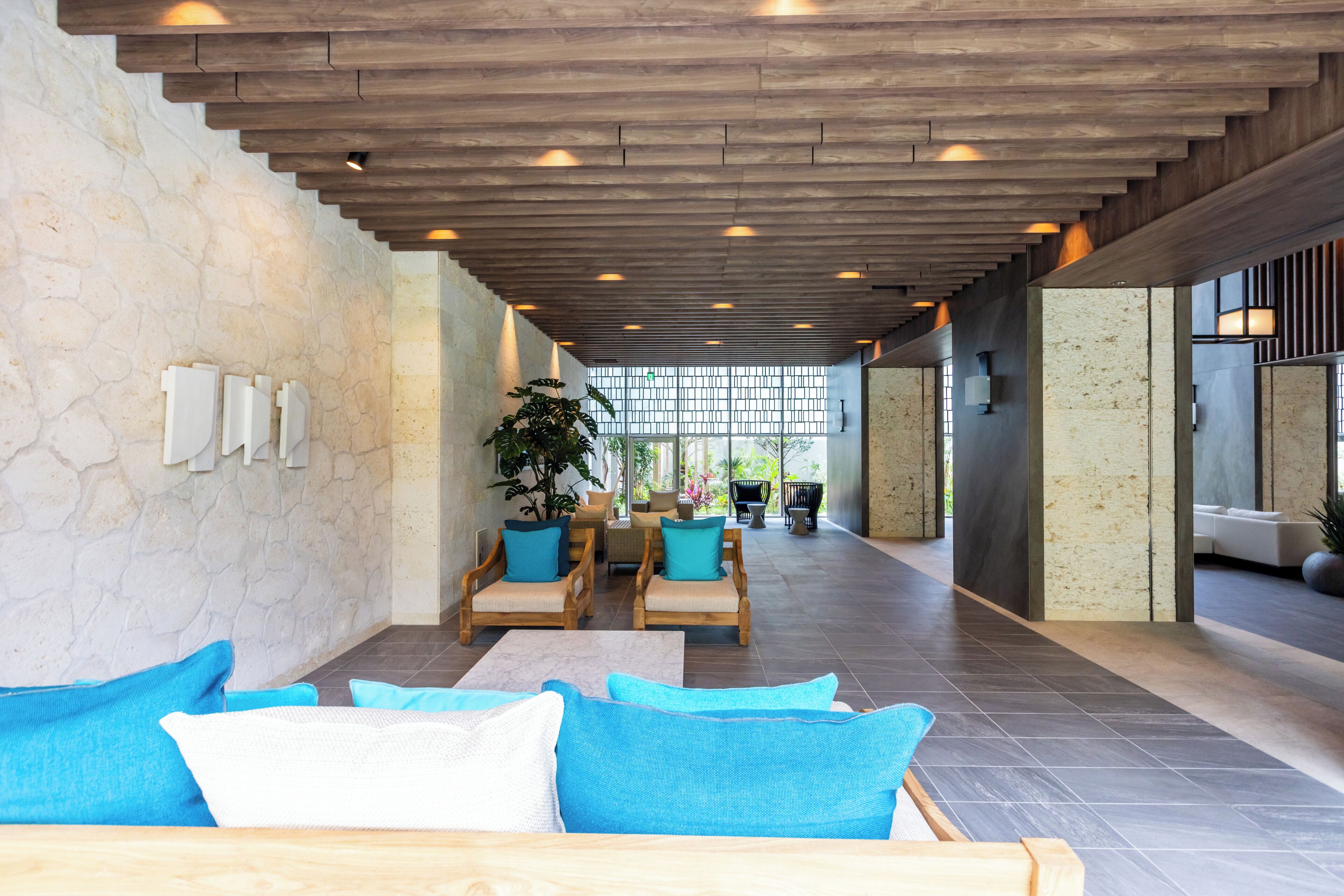 Un hall d’entrée spacieux avec un plafond haut, des poutres en bois et un coin salon agrémenté de coussins bleus.
