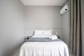 Ein Hotelzimmer mit Bett, Nachttisch, Wandklimaanlage und Vorhang.