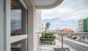 Un balcon donnant sur une rue, des palmiers et des immeubles.