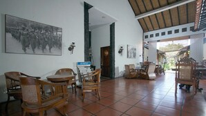 Een ruime kamer met betegelde vloer, houten meubels en een grote ingelijste foto aan de muur.
