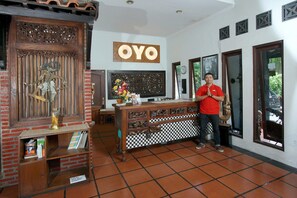 Un espace d’accueil avec un comptoir de réception en bois, une enseigne fixée au mur portant l’inscription « OYO », et un sol carrelé.