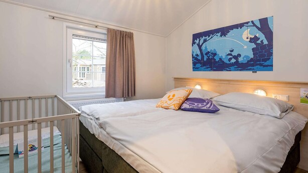 Een slaapkamer met een eenpersoonsbed, een ledikant, een raam met gordijnen en een kunstwerk aan de muur.