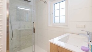 Een moderne badkamer met een douchecabine van glas, een wit wastafelmeubel en een raam voor natuurlijk licht.