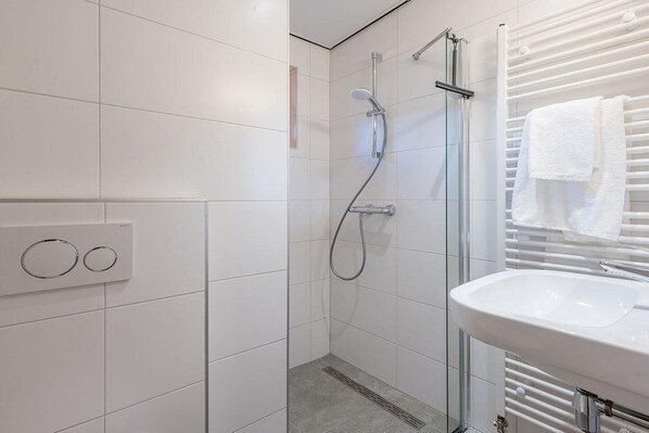A modern bathroom with a glass-enclosed shower, a white sink, and a towel rack.