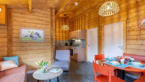 A cozy cabin interior with a dining table set for two, a kitchen area, and a living space with a sofa and a small round table. - Holiday home in Hoogerheide with shared pool (Hoogerheide)