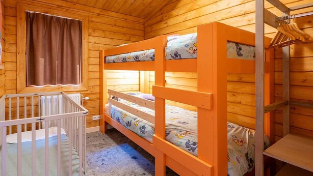 A wooden cabin room with bunk beds, a crib, and a window with curtains. - Holiday home in Hoogerheide with shared pool (Hoogerheide)