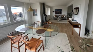 Ein modernes Wohnzimmer mit einem Glastisch, Holzstühlen, einer Couch und einem Couchtisch.