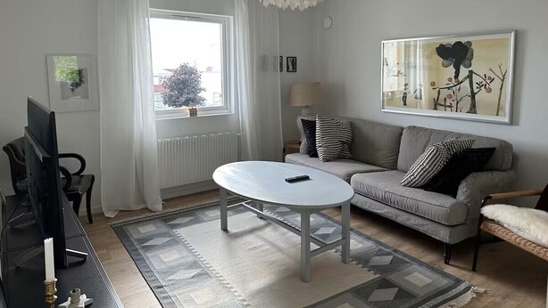 Ein Wohnzimmer mit einer Couch, einem runden Couchtisch, einem Fernseher und einem großen Fenster mit Vorhängen.