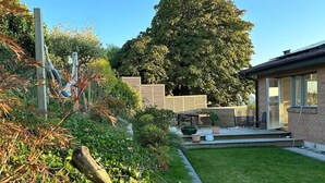 Ein Wohnhaus mit gepflegtem Rasen, einer Terrasse und Gartenmöbeln sowie einem großen Baum, der Schatten spendet.