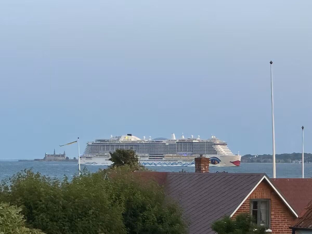 Ein großes Kreuzfahrtschiff liegt im Hafen fest, mit freiem Blick auf das Meer und ein entferntes Gebäude.