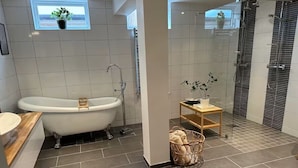 Ein modernes Badezimmer mit einer freistehenden Badewanne, einem Holzwaschtisch, einem kleinen Tisch mit Pflanze und einer Duschkabine.