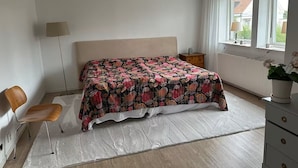 Ein Schlafzimmer mit Bett, Stuhl, Kommode, Lampe und Fenster.