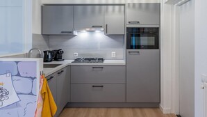 Una cocina moderna con armarios grises, horno integrado, cocina a gas y lámpara colgante.