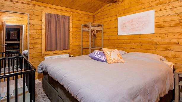Une pièce de cabane en bois comprenant un lit, une fenêtre avec des rideaux, un radiateur et un plafond en bois.