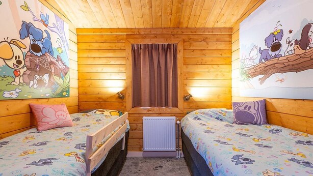 Una habitación tipo cabaña acogedora, con dos camas, paredes de madera y ropa de cama con motivos de dibujos animados.