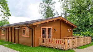 Una cabaña de madera con terraza amurallada, un camino de ladrillo y un entorno natural.
