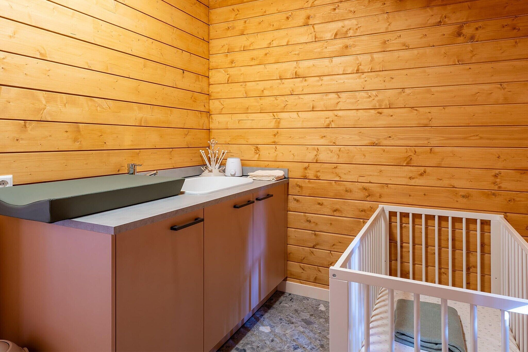Ein Holzblockhaus-Interieur mit einer Küchenzeile, einem Spülbecken und einem Babybett.
