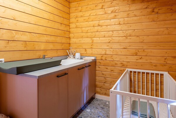 A wooden cabin interior with a kitchenette, a sink, and a crib.