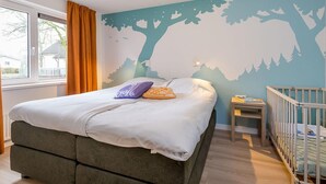 Ein Schlafzimmer mit einem Bett, einem Nachttisch, einem Babybett, einem Fenster mit Vorhängen und Wandmalerei.