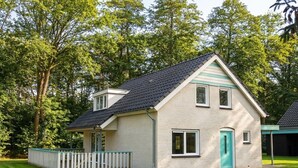 Ein zweistöckiges Haus mit geneigtem Dach, einer Veranda und einem eingezäunten Garten.