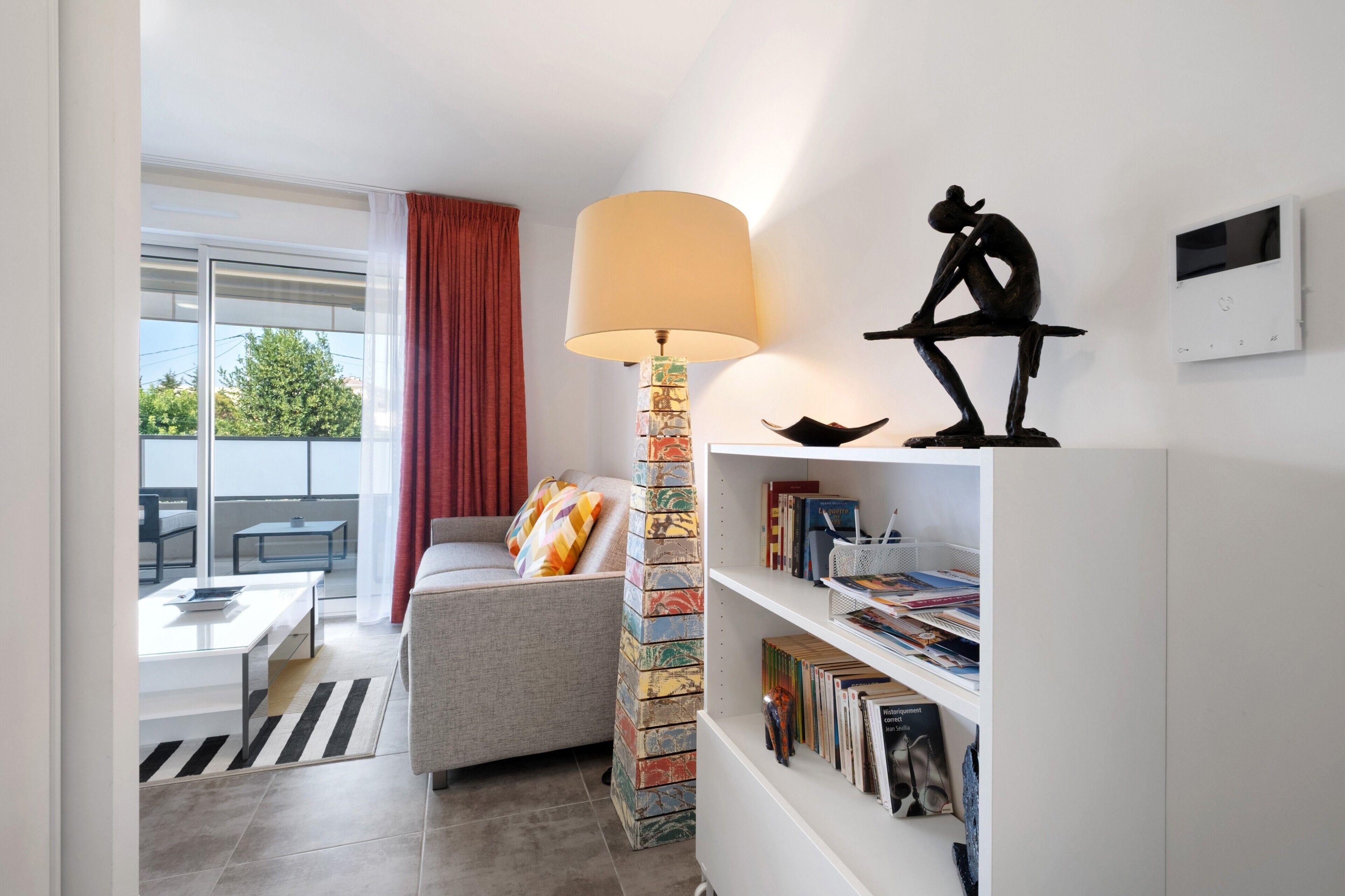 Een moderne woonkamer met een bank, een lamp, een boekenkast en een raam met uitzicht.