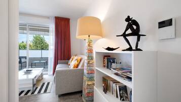 Een moderne woonkamer met een bank, een lamp, een boekenkast en een raam met uitzicht.