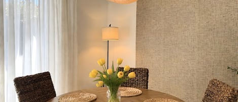 Ein runder Esstisch mit gewebten Platzsets, einer Vase mit gelben Blumen und einer hängenden Webdekorleuchte.