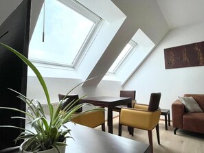 Um espaço de estar moderno com um clarabóia, uma mesa de jantar, cadeiras amarelas e um sofá castanho.