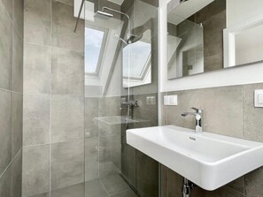 Ein modernes Badezimmer mit Dusche, einem großen Spiegel und einem weißen Waschbecken.