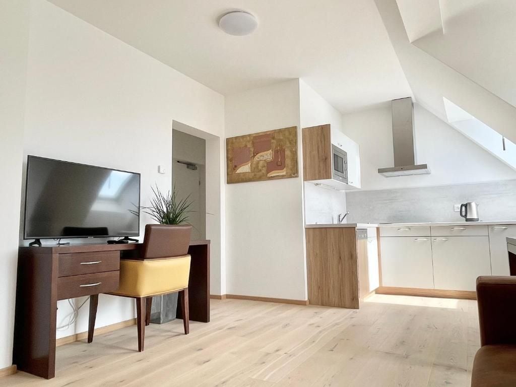 Ein modernes Wohnzimmer mit Flachbildfernseher, Schreibtisch und Sessel. Es gibt eine Küchenzeile mit Schränken und einer Mikrowelle.