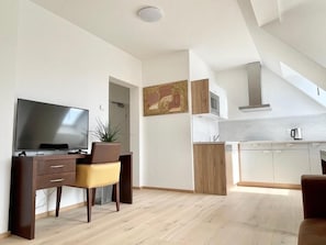 Una sala moderna con televisor de pantalla plana, un escritorio y una silla. Cuenta con una zona de cocina con armarios y un microondas.