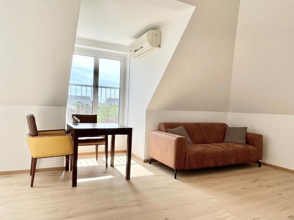 A room with a dining table and chairs, a sofa, and a large window with a view.