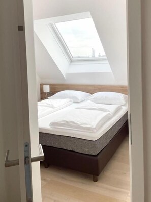 Un dormitorio con tragaluz, una cama con ropa blanca y cabecera de madera.