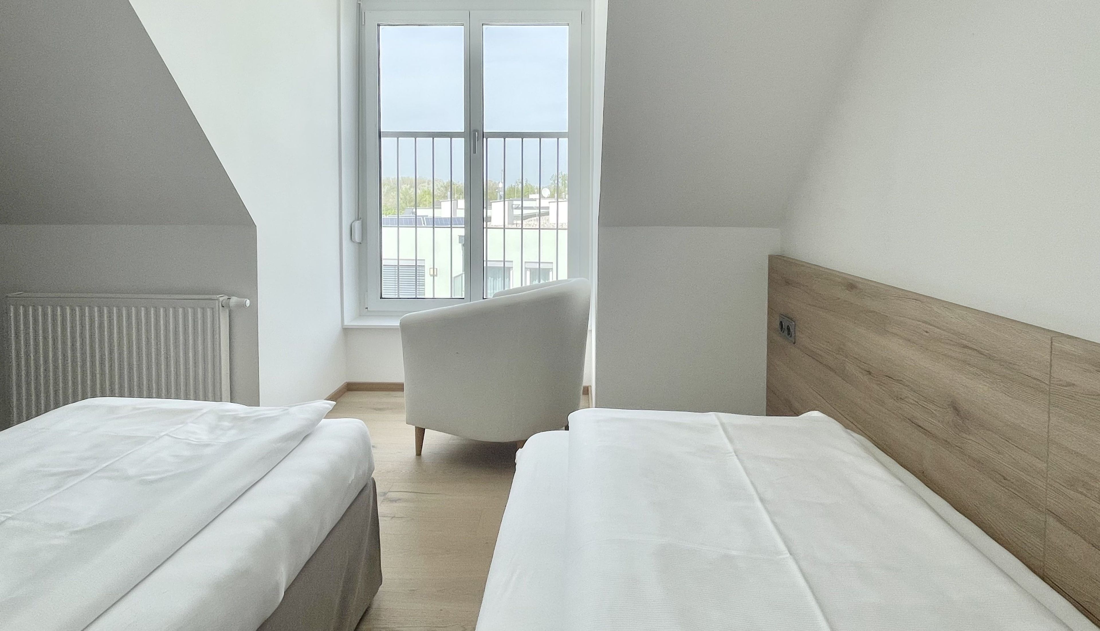 Quarto com duas camas, um radiador, uma janela com vista e uma cadeira.