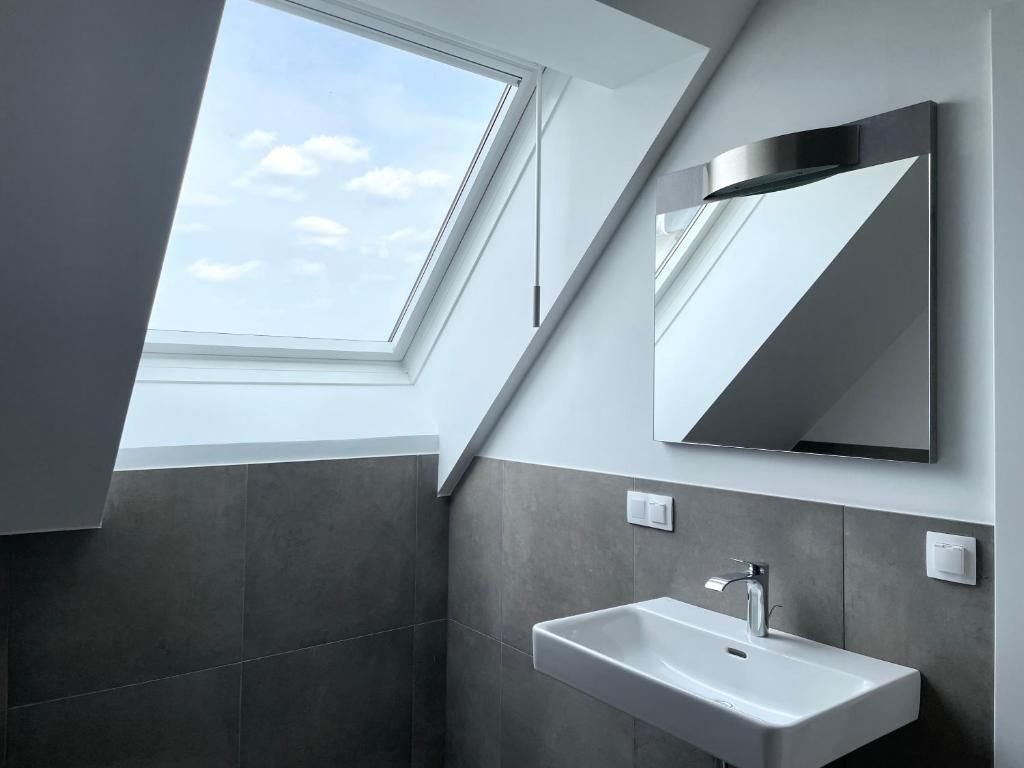 Un baño moderno con tragaluz, un espejo grande y un lavabo blanco.