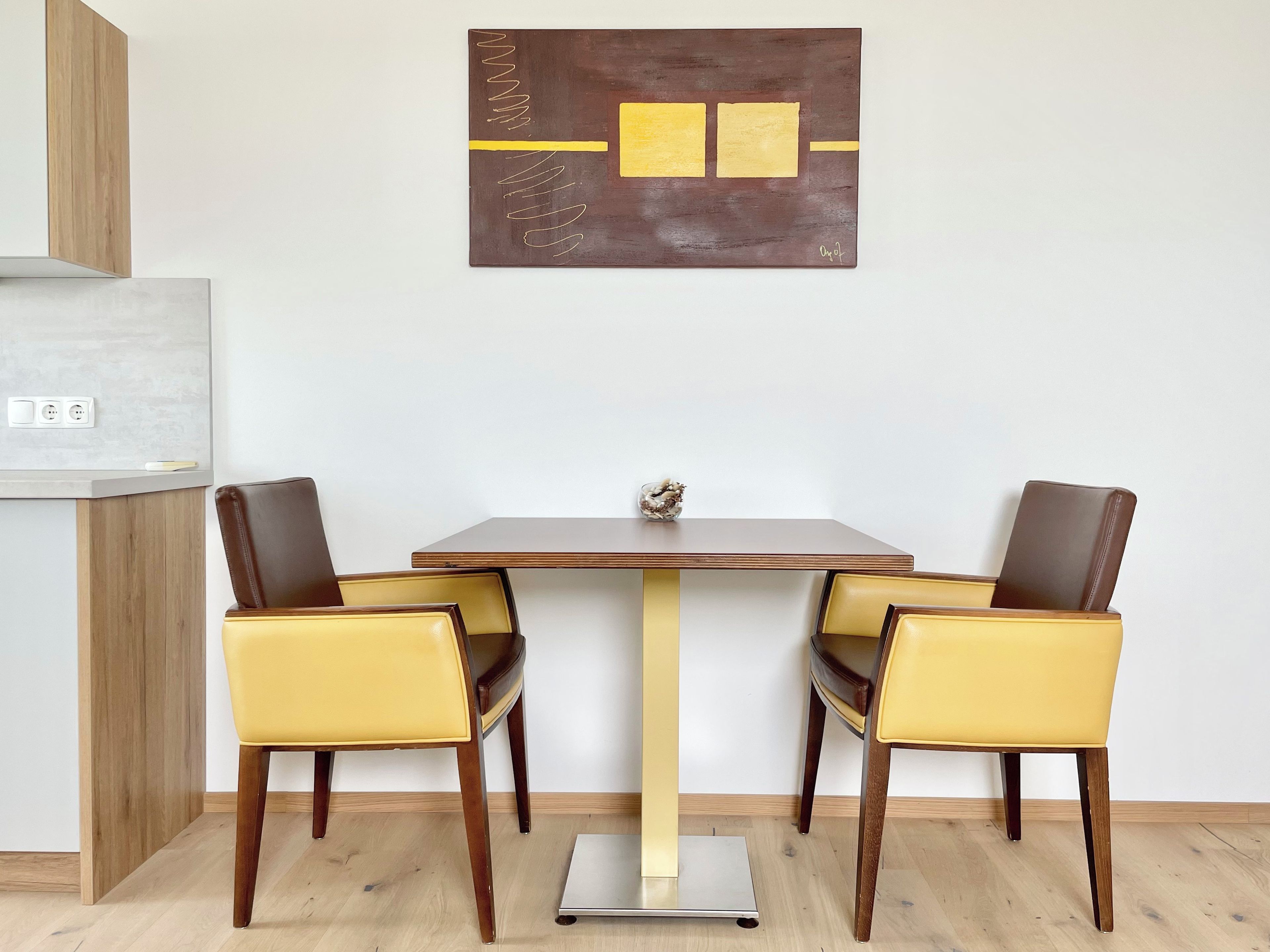 A dining area with a table and chairs, a wall-mounted artwork, and a kitchen counter with a scale.