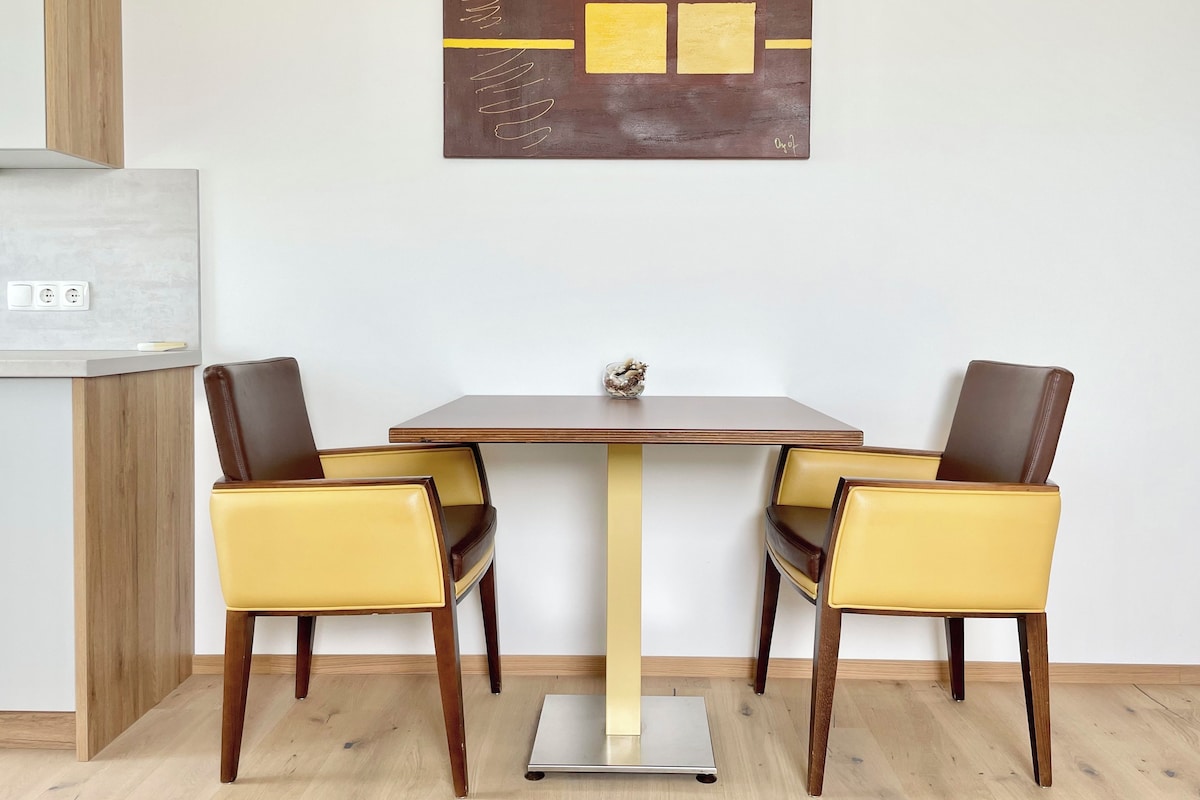 Un comedor con una mesa y sillas, una obra de arte colgada en la pared y una encimera de cocina con una balanza.