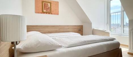 Un dormitorio moderno con cama, mesita de noche, lámpara y ventana con vistas.