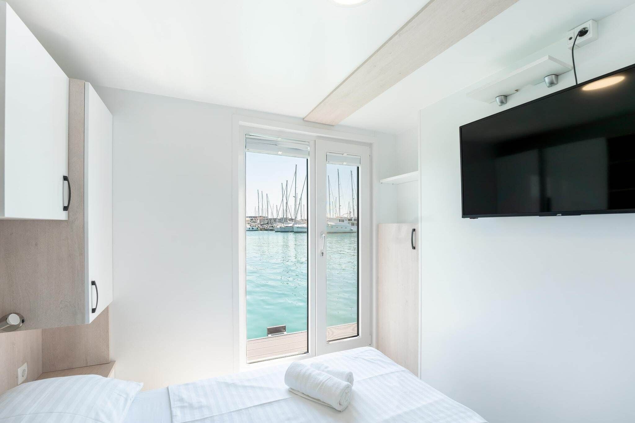 Habitación de hotel moderna con cama, televisión y vista hacia un puerto deportivo con barcos.