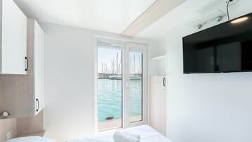 Habitación de hotel moderna con cama, televisión y vista hacia un puerto deportivo con barcos.