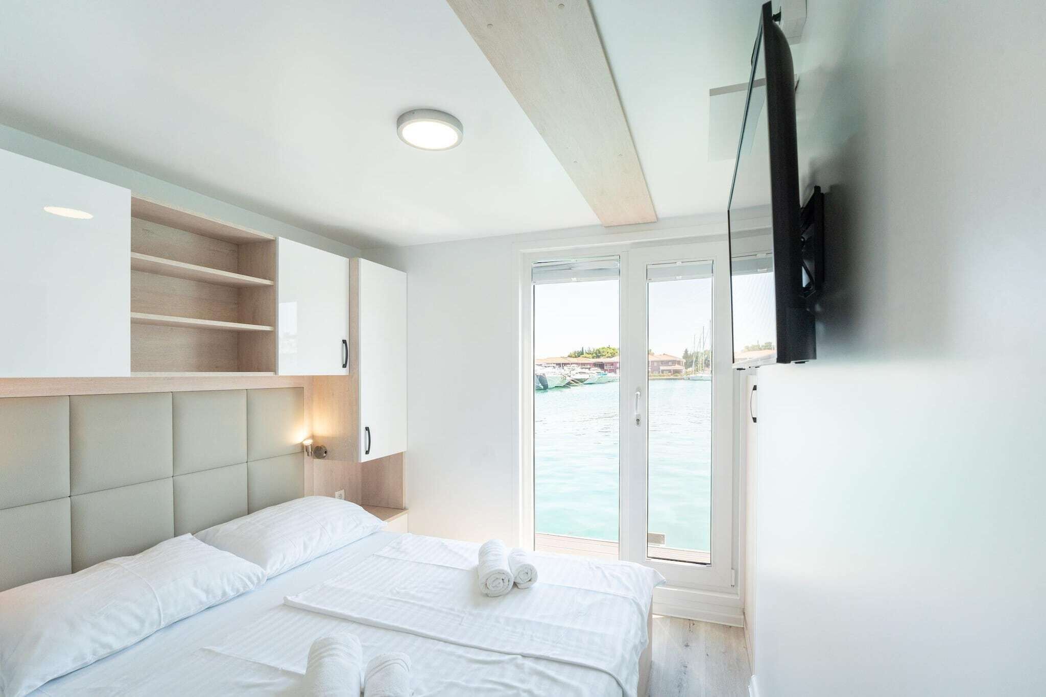 Habitación de hotel con cama, televisor montado en la pared y vista al mar a través de un ventanal grande.